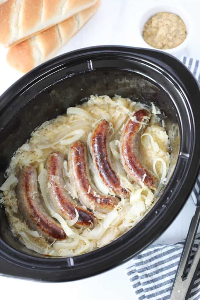 slow cooker brats after cooking on a white background next to buns and mustard
