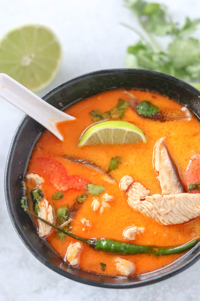 thai coconut soup with garnishes like chilis and lime in a bowl with a white spoon