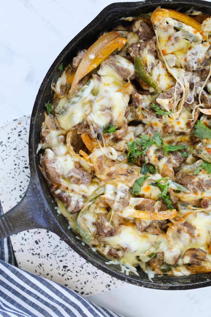 philly cheesesteak cassserole in a cast iron skillet on a white backrground