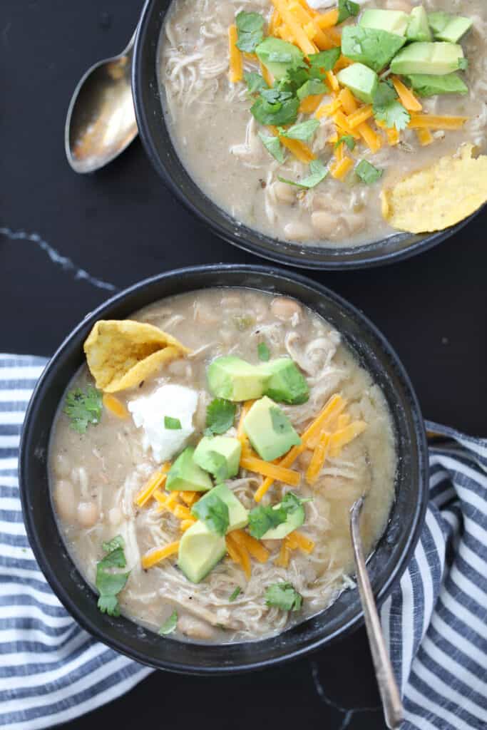 white bean chicken chili instant pot recipe in black bowls with cheese