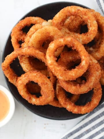 air fryer frozen onion rings on a black plate after cooking