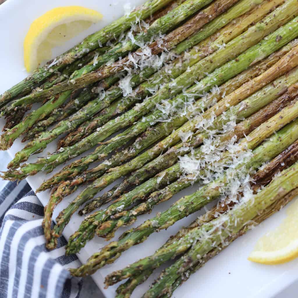 asparagus in air fryer topped with parmesan on a white plate
