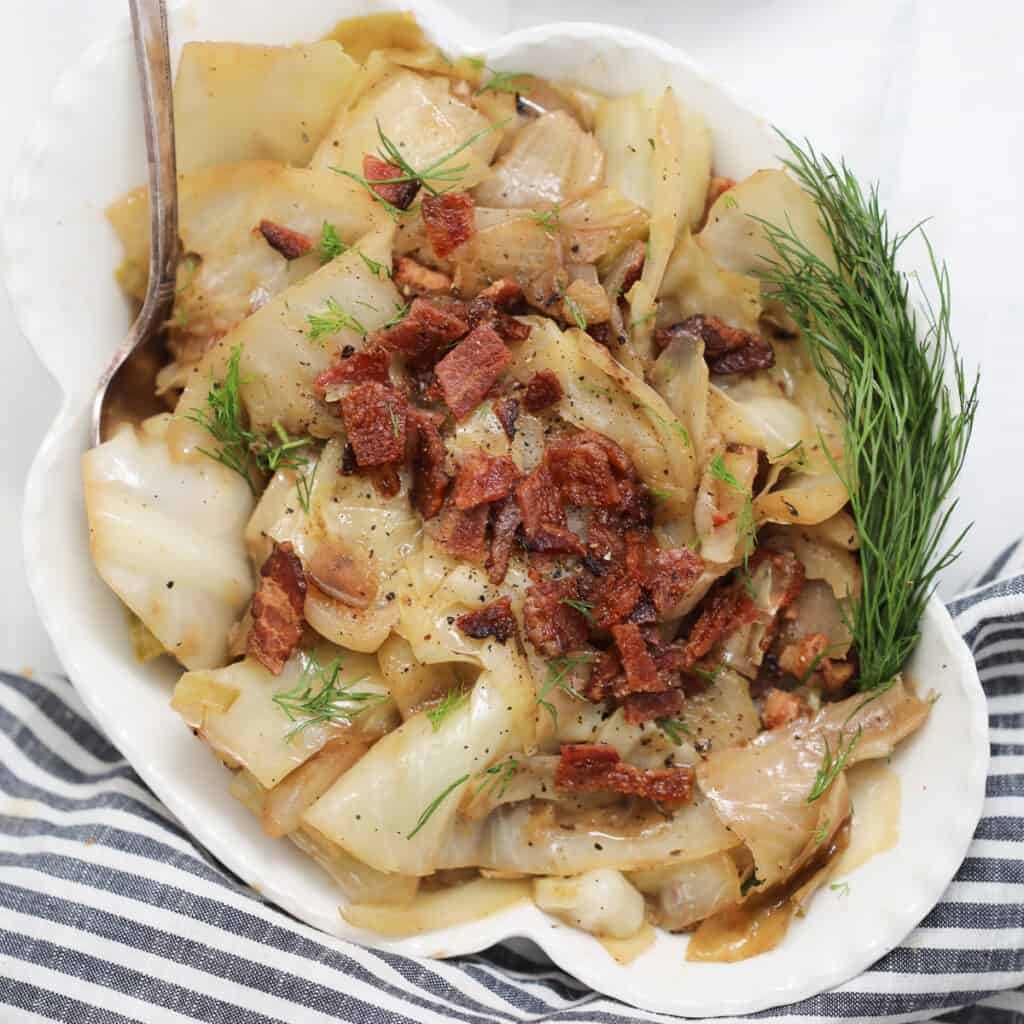 crock pot cabbage in a white bowl garnished with dill and bacon
