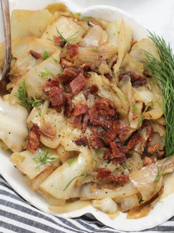 crock pot cabbage in a white bowl garnished with dill and bacon