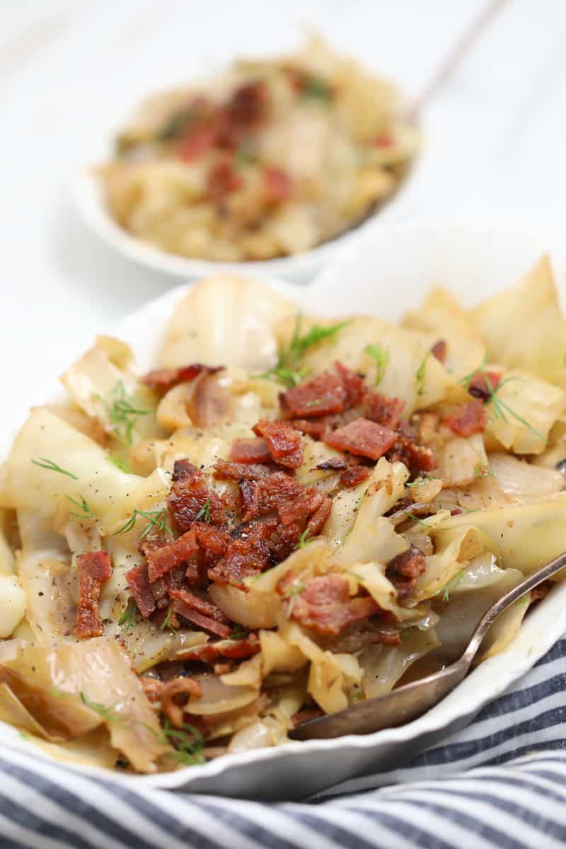 crockpot cabbage in a white serving dish garnished with bacon