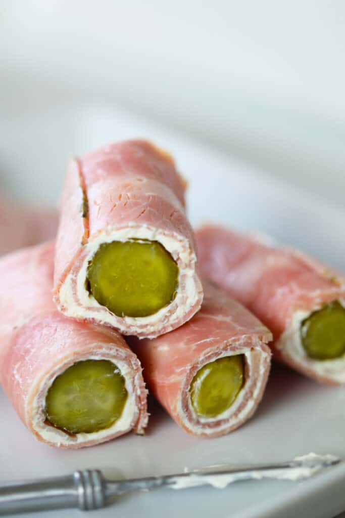 ham and pickle roll-ups stacked on a white plate