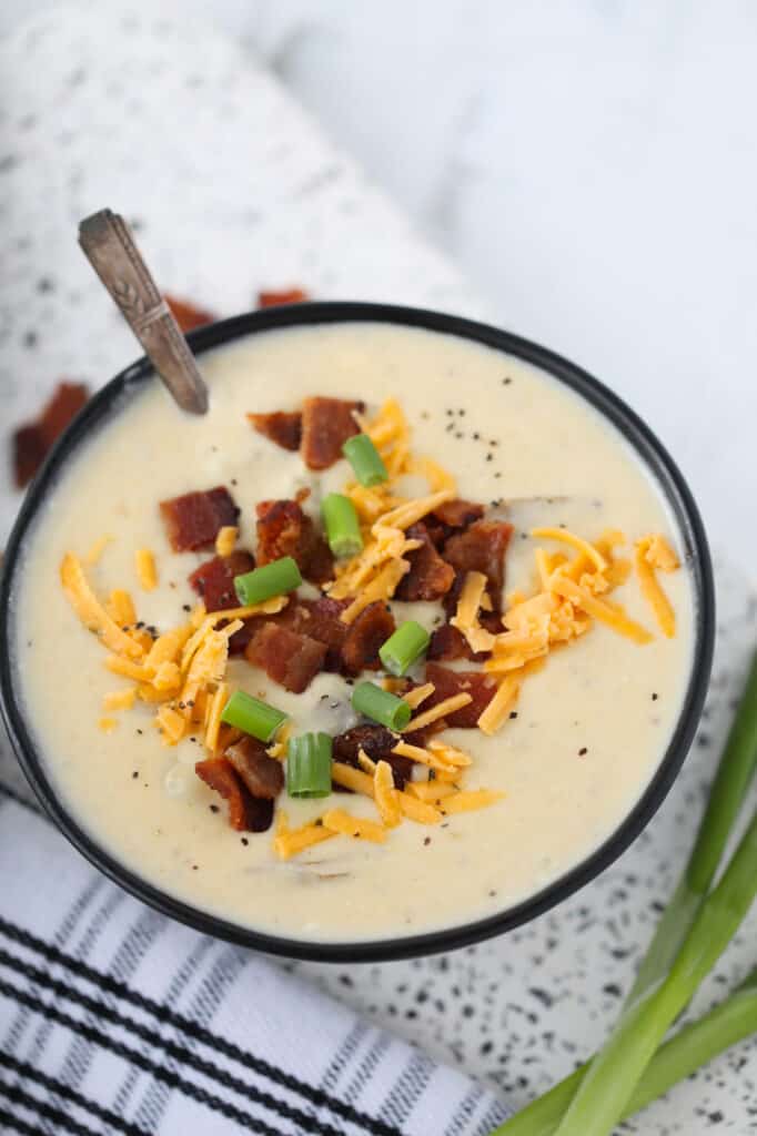 instant pot loaded potato soup in a black bowl with bacon and cheese garnishes