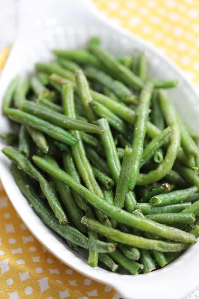air fryer frozen green beans in a white serving dish with a yellow cloth