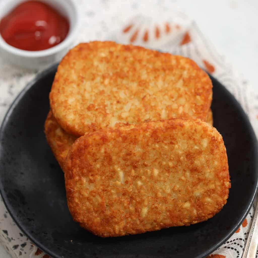 air fryer frozen hash browns on a black plate with ketchup