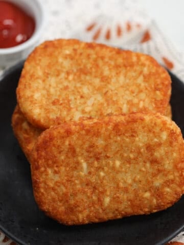 air fryer frozen hash browns on a black plate with ketchup