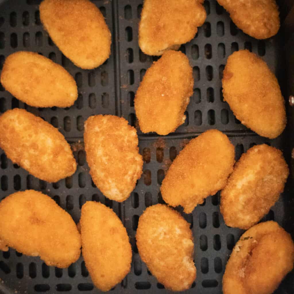 air fryer frozen jalapeno poppers getting placed in an air fryer before cooking