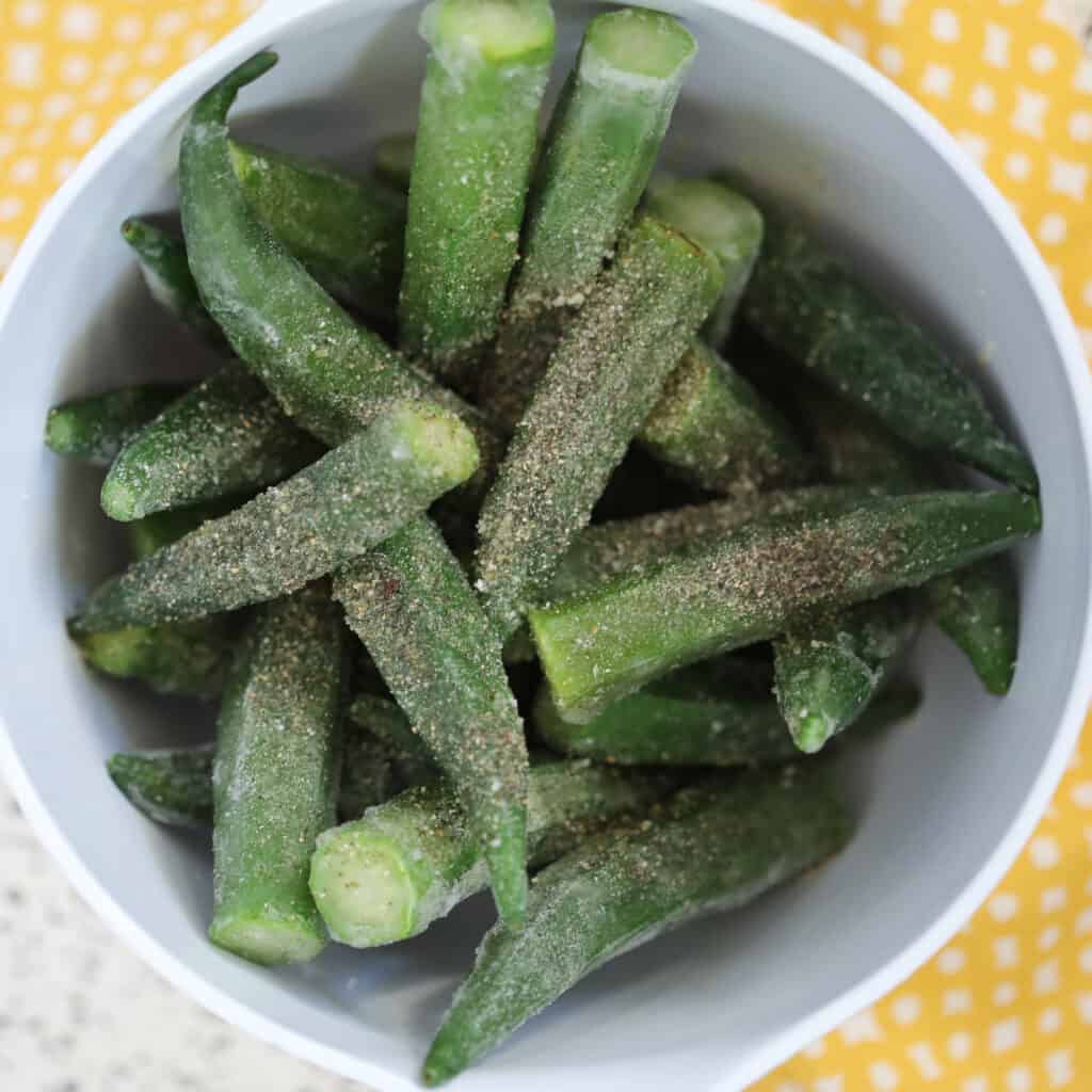 air fryer okra frozen mixed with seasoning in a white bowl