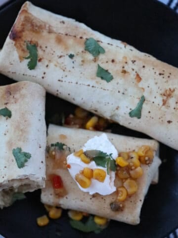 the cooked frozen burritos in air fryer after cooking with salsa and cilantro on a black plate