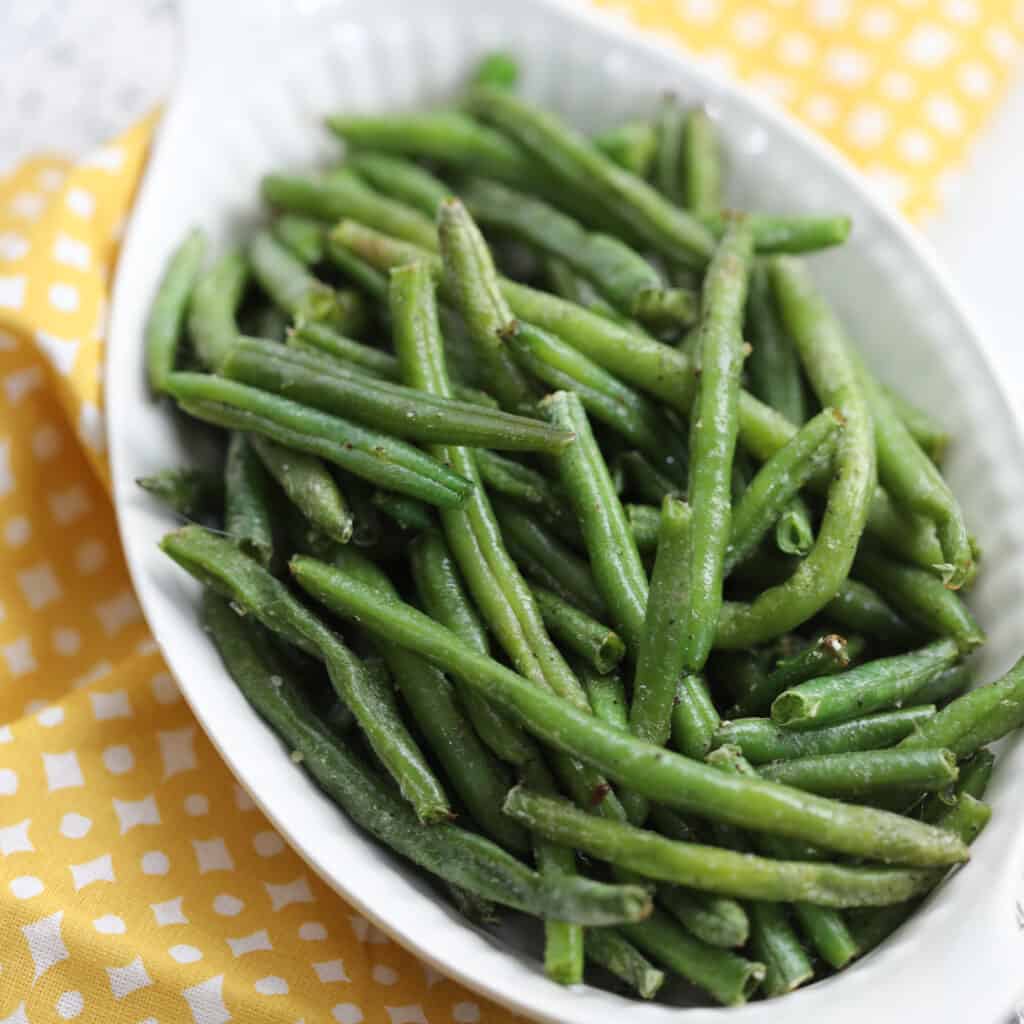 frozen green beans in air fryer ready to serve in a white dish that are healthy 