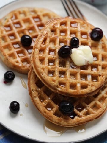 the frozen waffles in air fryer on a white plate with blueberries butter and syrup