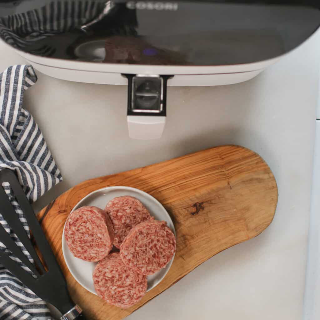 air fryer breakfast sausage patties next to the air fryer ready to be cooked