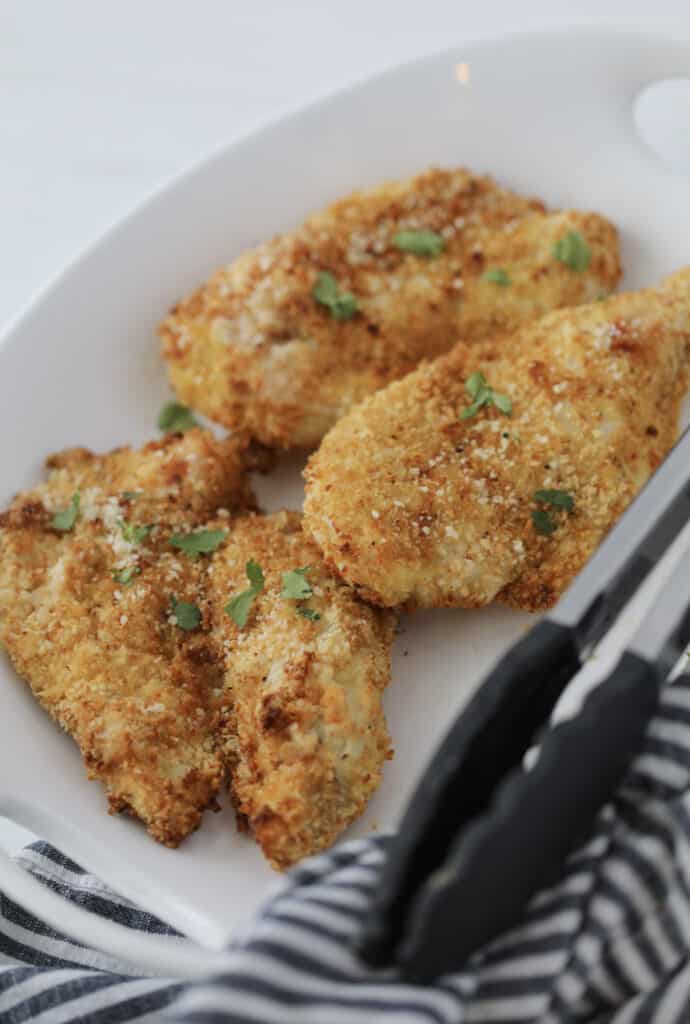 breaded chicken cutlets in air fryer after cooking on a white platter