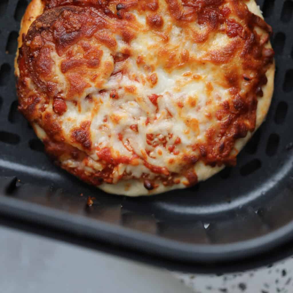 air fryer frozen pizza after cooking with melted browned cheese still in the air fryer