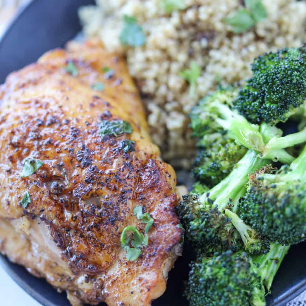 cooked chicken thighs in a pan served with broccoli and rice
