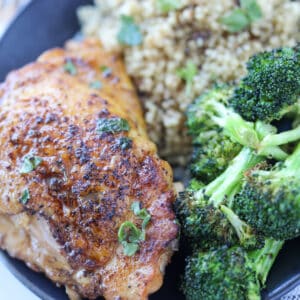 cooked chicken thighs in a pan served with broccoli and rice