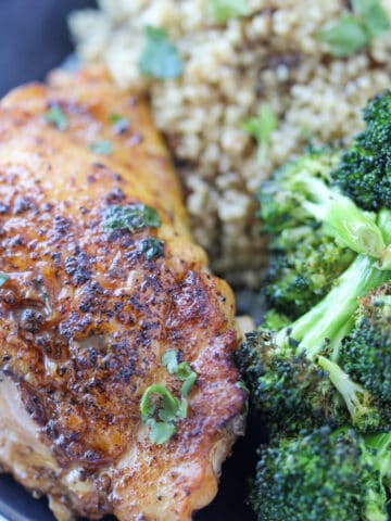 cooked chicken thighs in a pan served with broccoli and rice