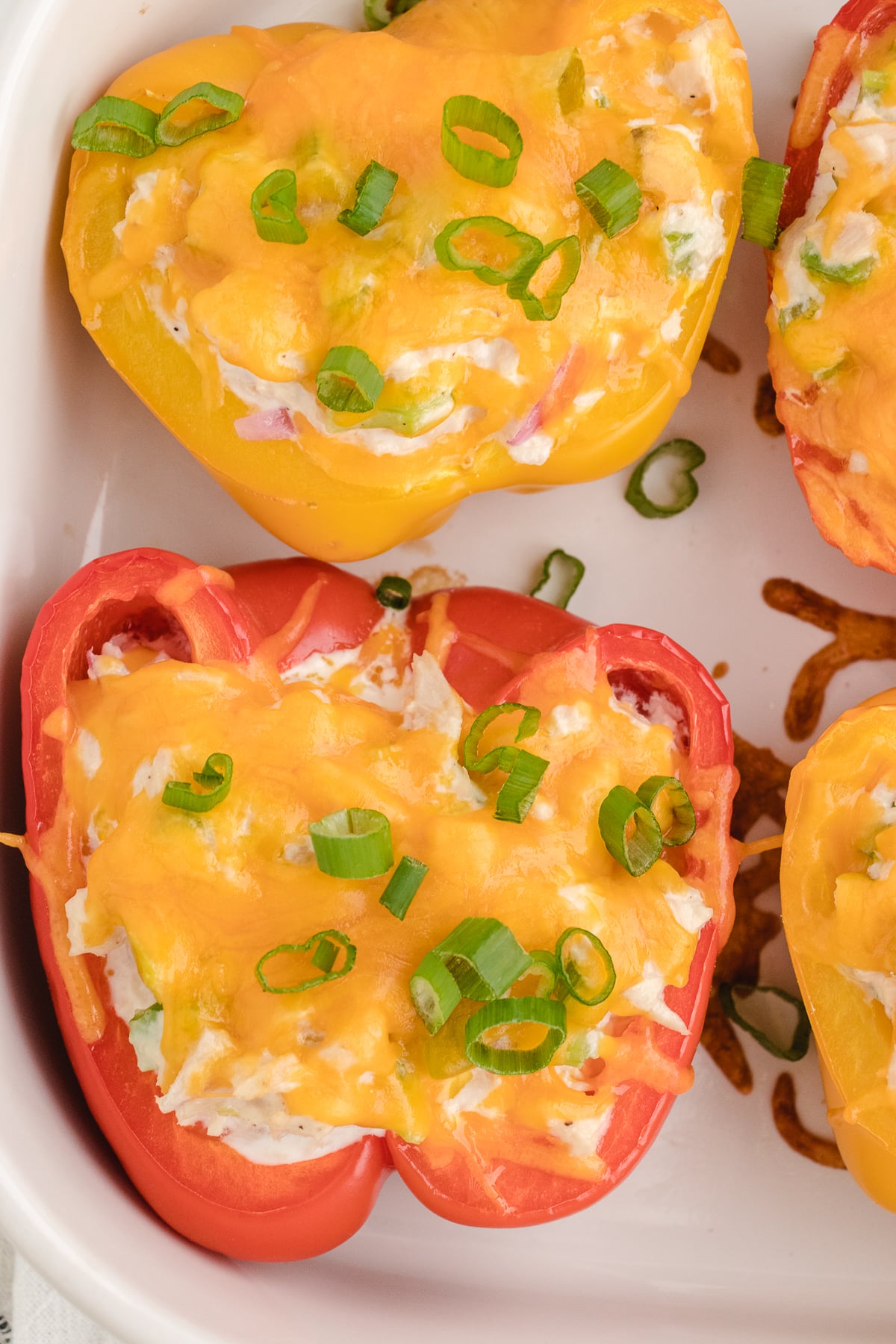 close up of bell peppers stuffed with tuna melt ingredients on a white baking dish after cooking