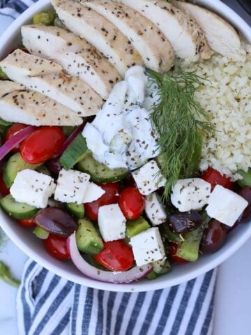 greek salad meal prep in a bowl with tzaziki sauce and cauliflower rice