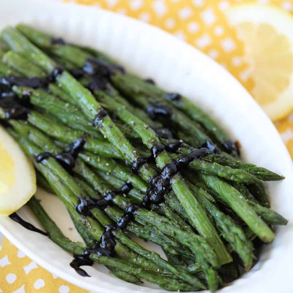 cooking frozen asparagus in an air fryer in a serving dish with lemon and balsamic