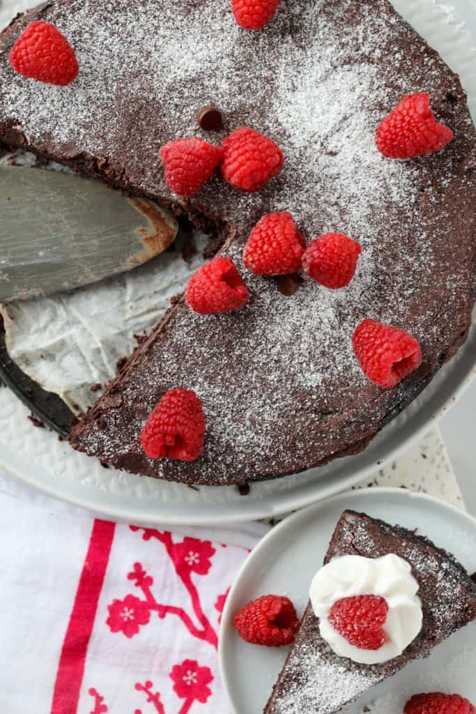 flourless chocolate cake with cocoa powder top down view with slice on a plate