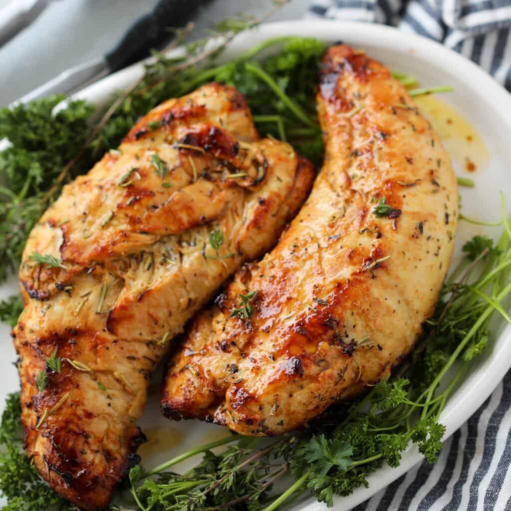 whole air fryer turkey tenders on a white platter with fresh herbs ready to carve for Thanksgiving dinner