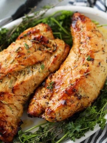 whole air fryer turkey tenders on a white platter with fresh herbs ready to carve for Thanksgiving dinner