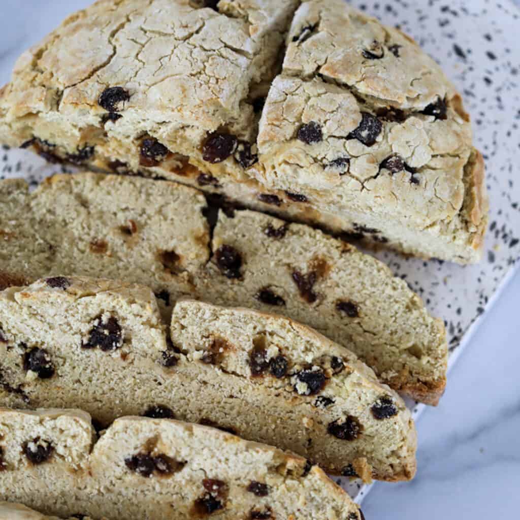 gf irish soda bread partially sliced with raisins on a white cutting board