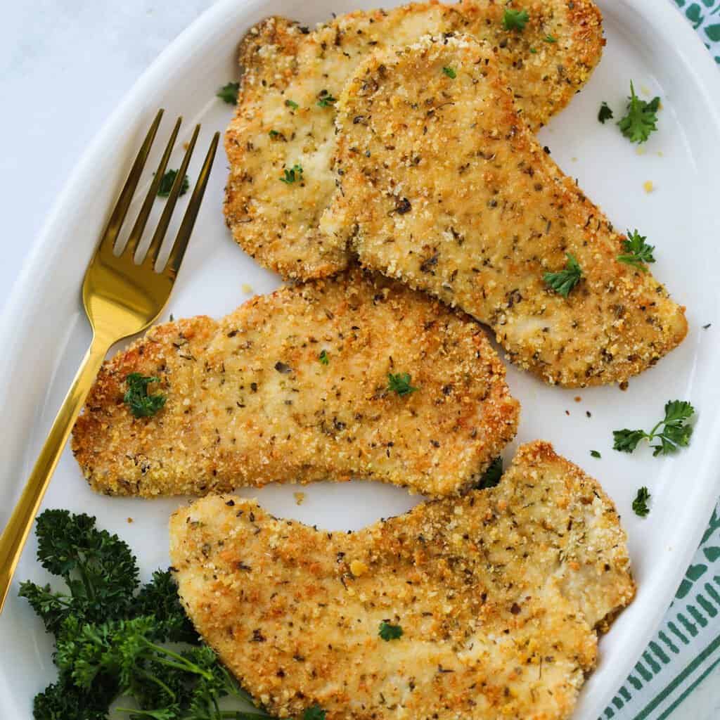 turkey cutlets in air fryer on a white plate sprinkled with parsley