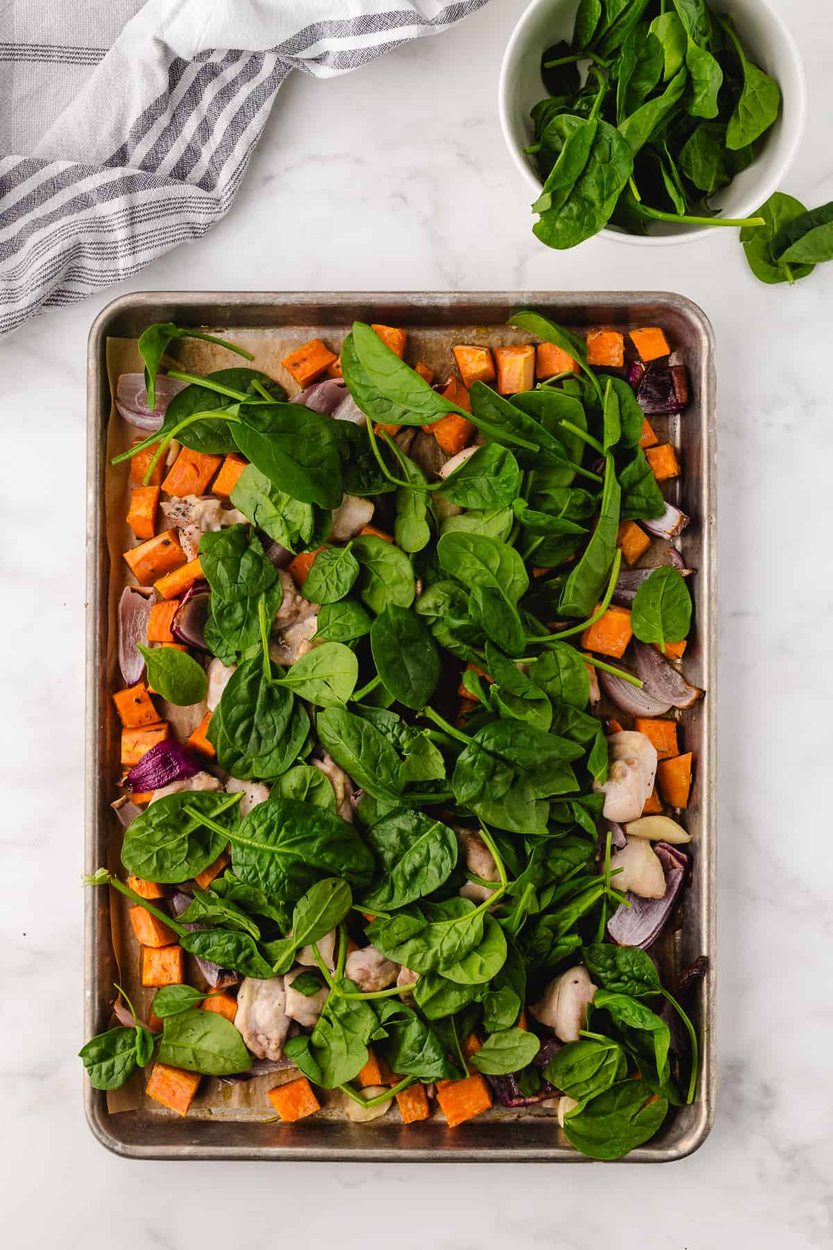 chicken thighs and sweet potatoes sheet pan recipe putting spinach on top