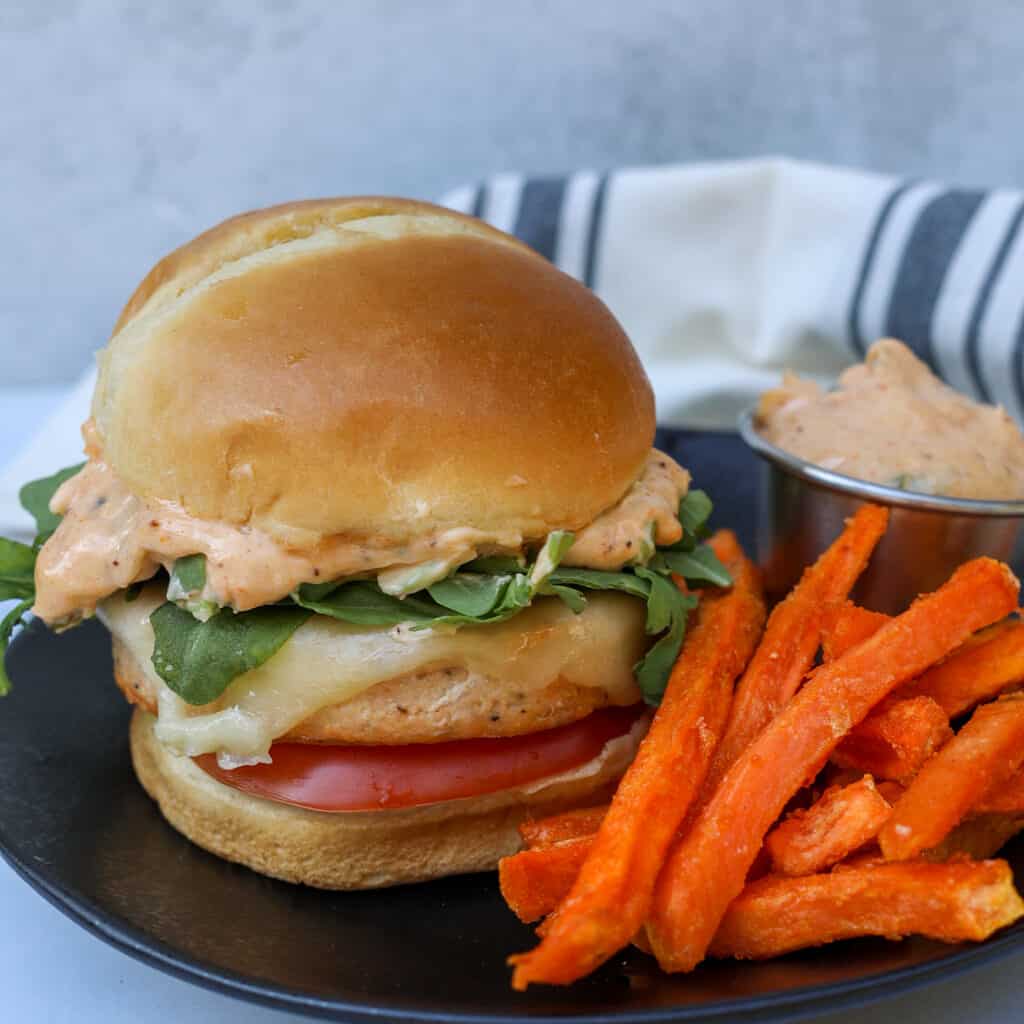 air fryer salmon burgers from frozen on a plate after cooking with sweet potato fries and sauce