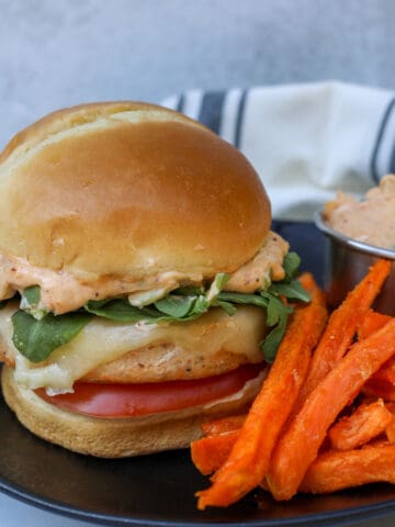 air fryer salmon burgers from frozen on a plate after cooking with sweet potato fries and sauce