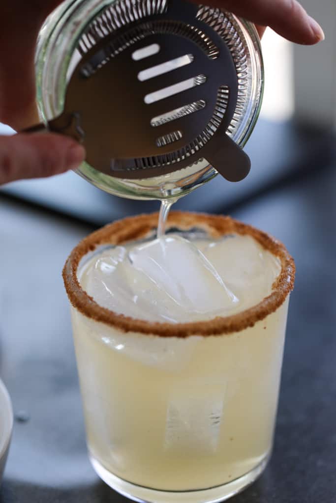 tequila and apple cider getting strained into a glass