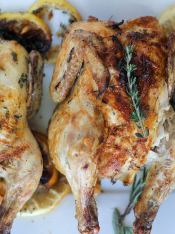 herb cornish hens air fryer recipe on a platter with fresh herbs and lemon