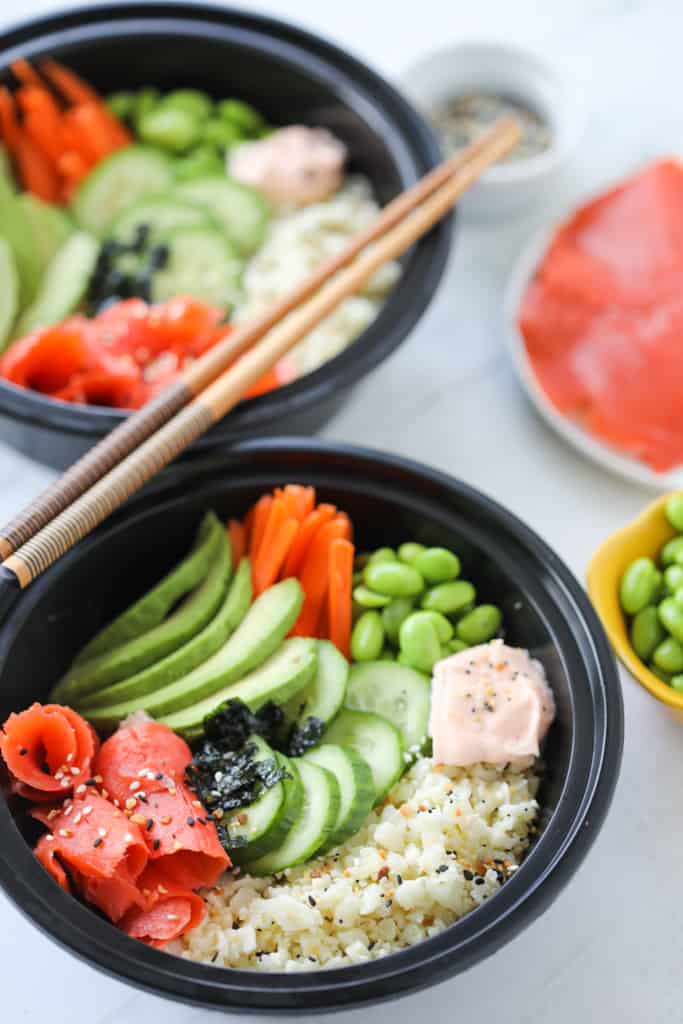 two salmon sushi bowls at a side angle with chopsticks in meal prep containers