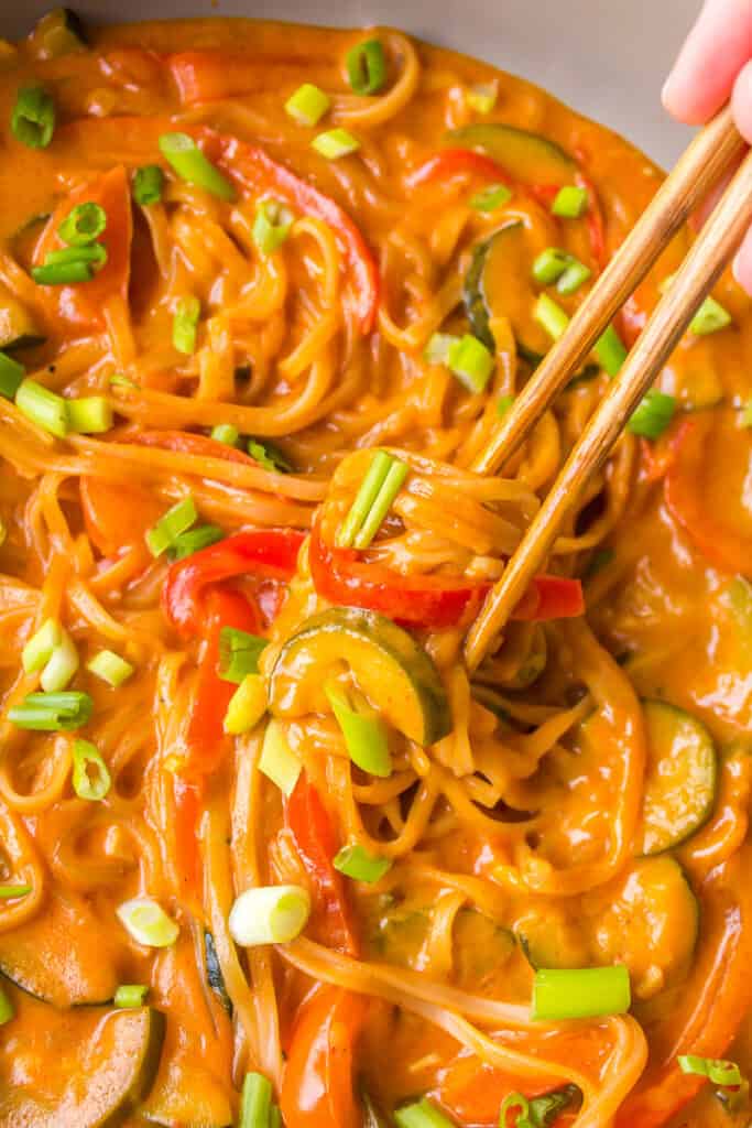 thai curry rice noodles with red curry sauce in a pan with chopsticks about to hold one bite