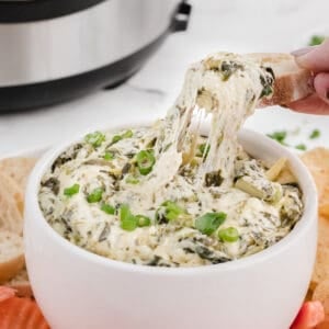 copycat Applebees spinach artichoke dip in a bowl with a cheese pull on bread