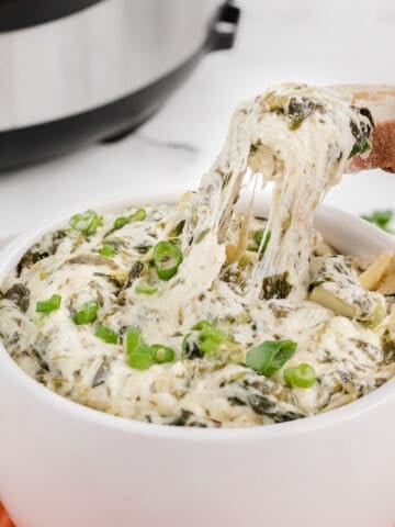 copycat Applebees spinach artichoke dip in a bowl with a cheese pull on bread