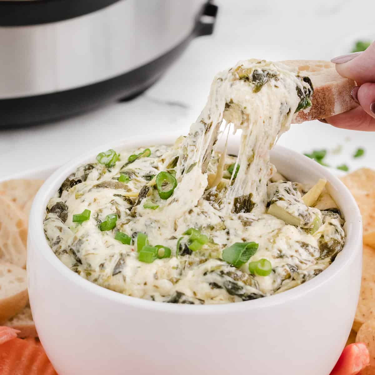 copycat Applebees spinach artichoke dip in a bowl with a cheese pull on bread