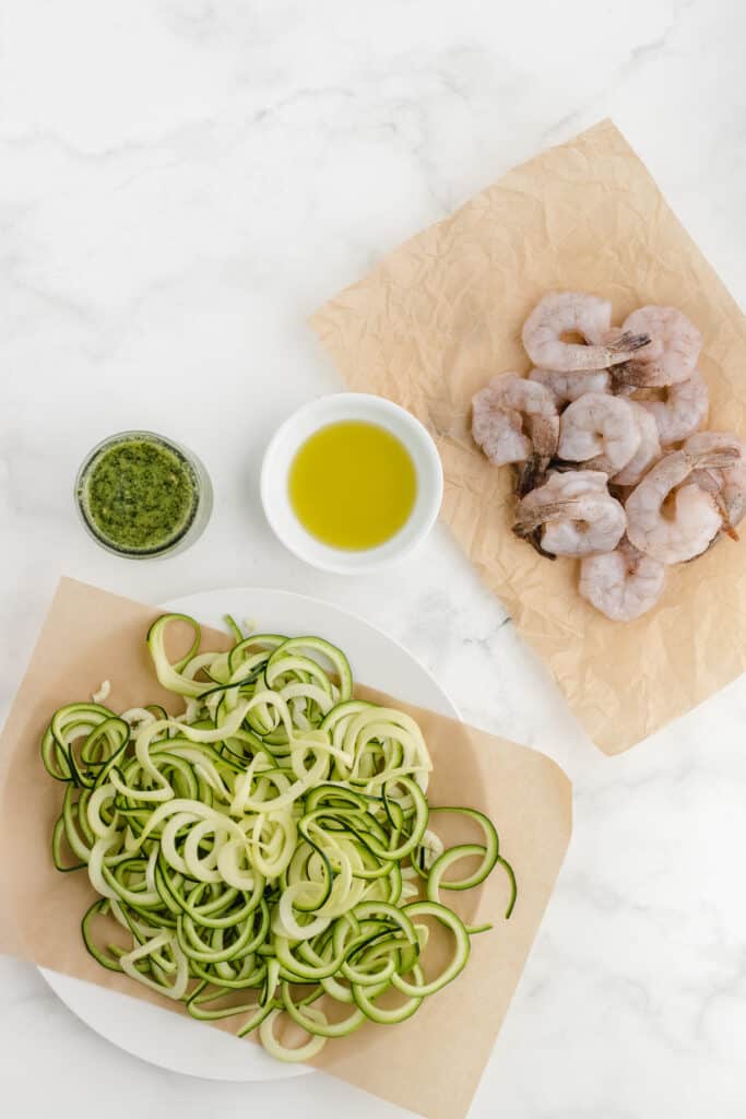 shrimp with zoodles and pesto ingredients on a white cutting board