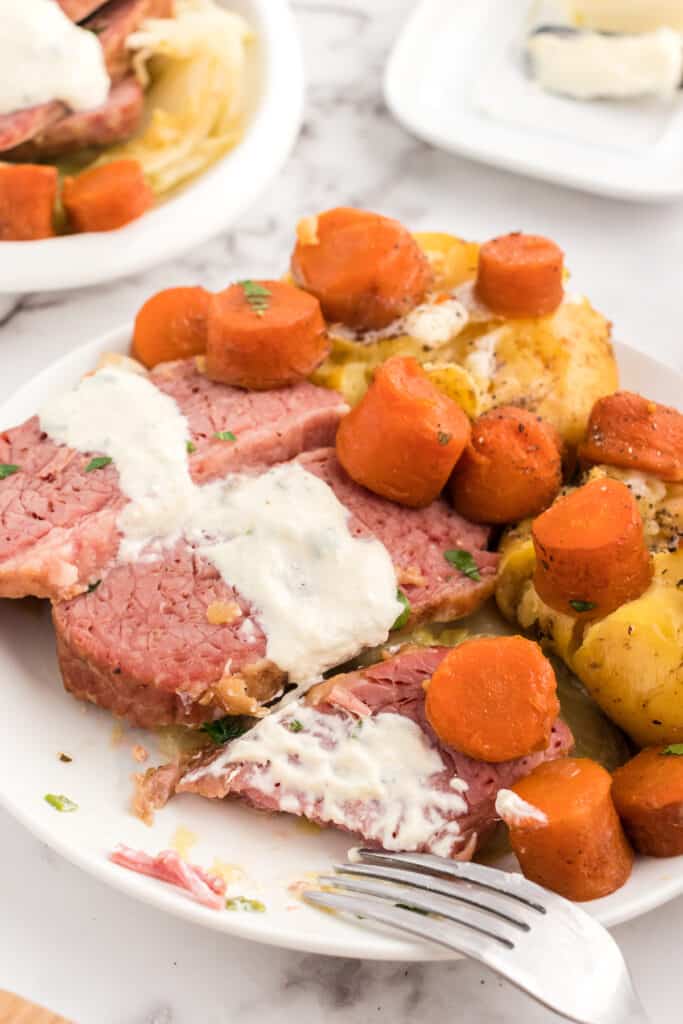 corned beef and cabbage plated and served topped with horseradish sauce.