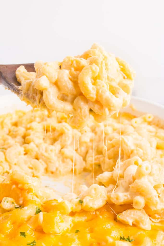 creamy baked mac and cheese with a cheese pull coming off of a wooden spoon