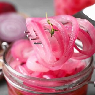 Pickled red onions being pulled from the jar with a fork.
