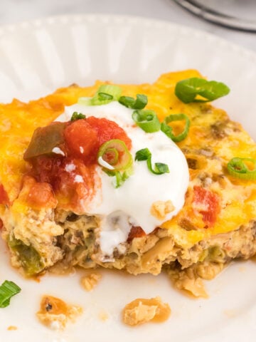 A square slice of keto breakfast casserole on a white plate topped with sour cream and salsa.
