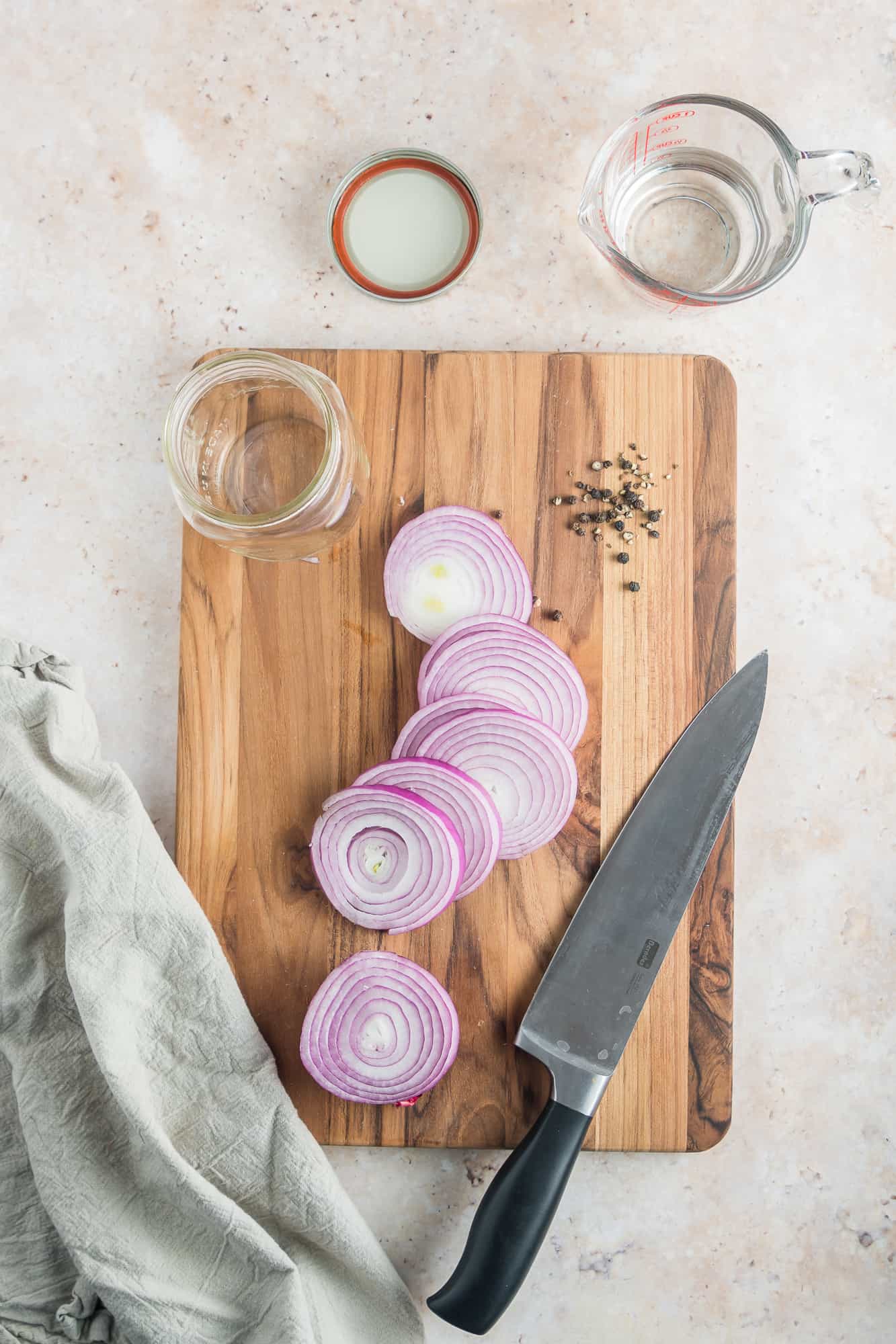 Sliced red onions on a cutting board with the rest of the ingredients and a sharp knife.