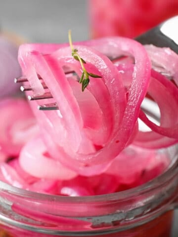 Pickled red onions being pulled from the jar with a fork.